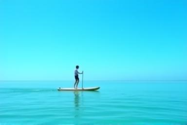 Person paddleboarding on calm water under a blue sky enjoying the peace
